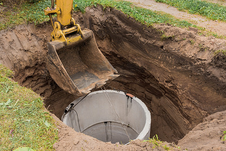 带桶的挖掘机，降低到钢缆混凝土下水道环上的坑中。