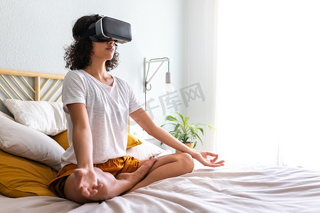 拉丁裔女性坐在床上借助 VR 体验应用进行冥想。