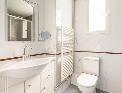 舒适明亮的白色浴室，铺有菱形瓷砖，带自然光马桶水槽窗、加热毛巾架和镜子。