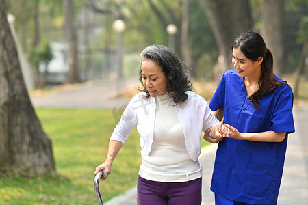 年轻有爱心的女护士帮助老年妇女在公园散步。