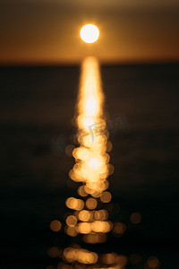 在模糊抽象模糊的日落背景上，明亮的黄色太阳圆盘在海水上投下眩光。