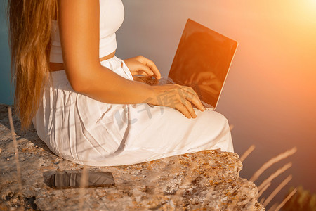 轻松愉快摄影照片_快乐的自由职业女性在笔记本电脑上打字，欣赏风景如画的海景，在轻松愉快的氛围中突出远程工作的理念。
