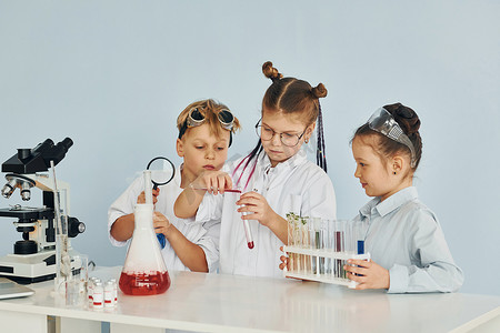 白大褂实验室摄影照片_穿白大褂的孩子们在实验室里用设备扮演科学家