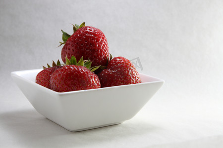 四个草莓放在一个白色的碗里，稍微靠左