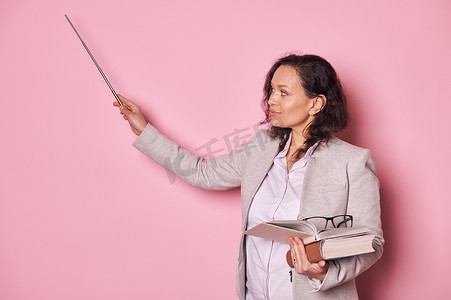 自信的中年女性，学校教师教授，在解释课程时将指针指向粉色墙上的复制空间