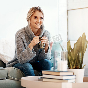 女人在客厅里放松，喝咖啡，微笑，在沙发上平静，在家里满足于生活方式和幸福。