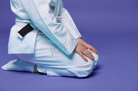 儿童跆拳道摄影照片_穿着白色和服的儿童合气道摔跤手的剪影，双手放在膝盖上，与紫色背景隔离，带有复制空间。