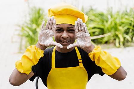 黑人厨师摄影照片_黑人非洲厨师少年双手捧着面粉，面带微笑。