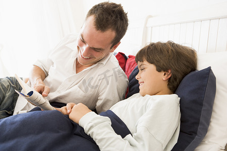 儿子给父亲摄影照片_男人在床上微笑着给小男孩看书