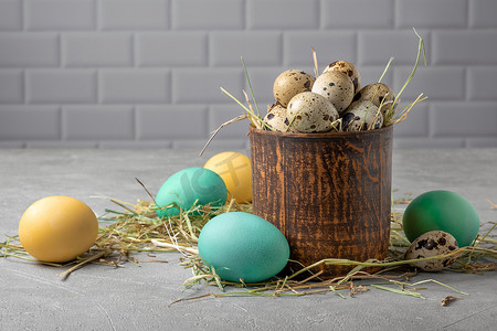 装饰彩绘摄影照片_干草中装有鹌鹑蛋的粘土容器，周围是彩绘鸡蛋
