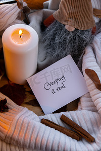 CREEPING IT 真实文本贺卡概念 在窗台上舒适的家中庆祝万圣节秋季假期 Hygge 美学氛围 秋叶侏儒香料和蜡烛在温暖的黄色灯光下的针织白色毛衣上