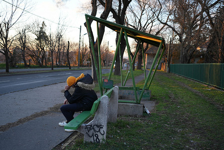 悲哀地摄影照片_坐在公共汽车站的年轻人悲伤地抱着他的头