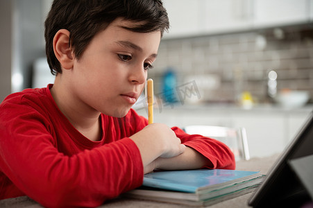 聪明的少年小学生解决数学问题，做家庭作业，使用数字平板电脑在家上在线课程