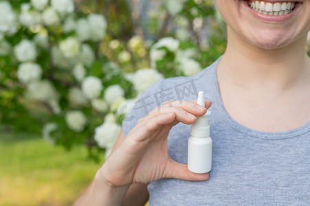 幸福的女人在一棵开花的树的背景下展示喷鼻剂。