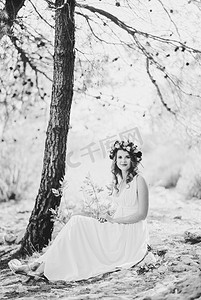 花环头戴摄影照片_头戴花环的新娘坐在一棵树下。