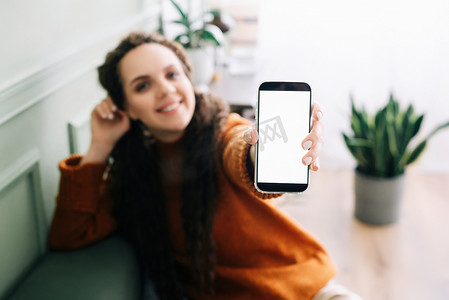 快乐的年轻女子手持手机展示手机显示屏，展示大白色空白蜂窝显示模板模型，用于数字应用程序促销广告的智能手机模型屏幕。