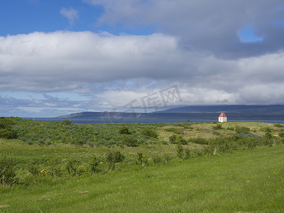 冰岛夏季风景，绿草如茵，地平线上的大海和悬崖，小房子和蓝天白云背景