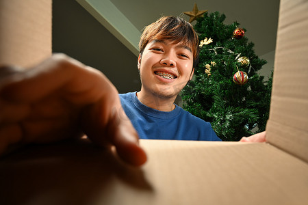 礼物盒子打开摄影照片_从盒子底部看，微笑的男人试图从未包装的盒子里拿礼物或包裹。
