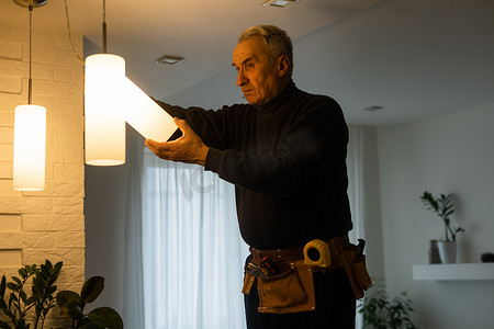 家杂摄影照片_换灯泡的老人：退休的男人做家务，更换灯泡和圆顶，巧妙地装饰。
