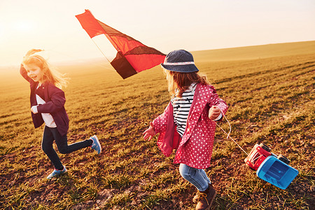 风筝玩具摄影照片_阳光明媚的白天，两个小女孩朋友在田野上玩风筝和玩具车