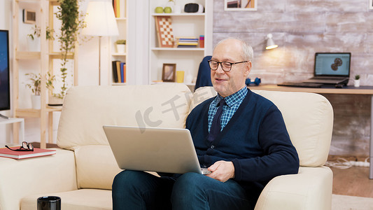 在笔记本电脑上进行视频通话时，一对戴眼镜的老年夫妇坐在沙发上。