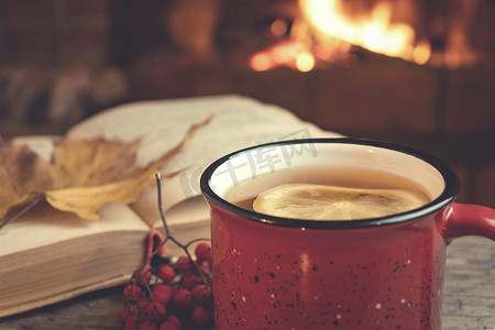 红杯配热茶，壁炉前放着一本打开的书，壁炉概念的舒适、放松和温暖