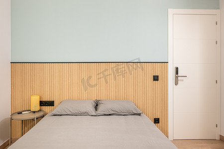 现代双人床摄影照片_双人床配有时尚的灰色床单、小床头柜和墙上的木制装饰板条。
