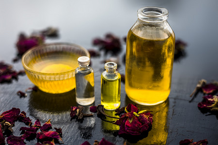 木质表面瓶子中的蓖麻油、茶树油和一些椰子油的特写，以及表面上还存在的一些生蜂蜜和玫瑰花瓣。