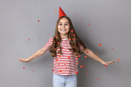 穿着衣服的小女孩张开双臂站在飘落的五彩纸屑下庆祝生日。