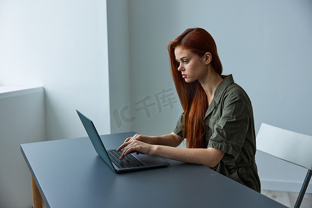 女性职工摄影照片_在明亮的办公室里全职工作的女性在笔记本电脑上打字时感到困惑