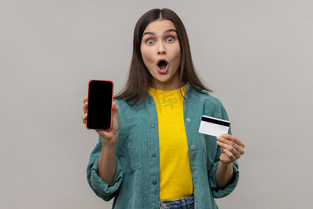 黑蜂窝摄影照片_拿着信用卡和黑屏智能手机的黑头发的惊讶女人。