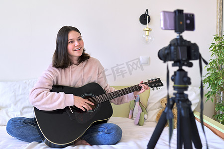 教育频道摄影照片_十几岁的女孩弹吉他，为频道录制视频，博客
