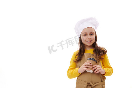 食堂外卖摄影照片_戴着厨师帽和围裙的可爱微笑的小女孩女服务员，拿着可回收纸杯里的外卖热饮