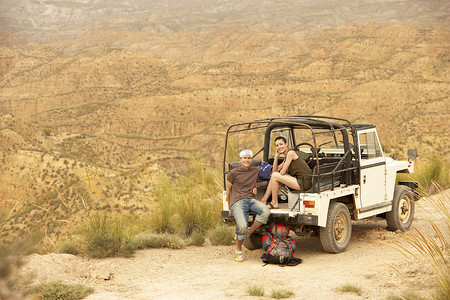 四轮驱动摄影照片_一对夫妇坐在沙漠悬崖边的四轮驱动汽车后面