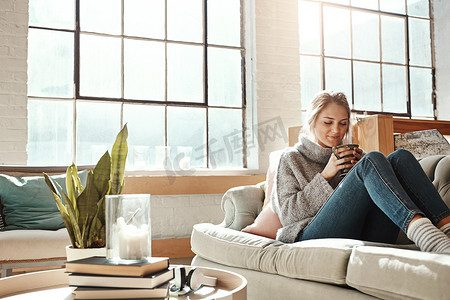 满足幸福摄影照片_女人在客厅里放松，在沙发上喝咖啡和平静，在家里满足于生活方式和幸福。