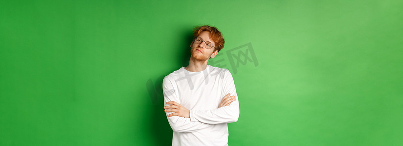 自信的年轻人，一头红发，戴着眼镜，在右侧的复制空间里自鸣得意，胸前自信地交叉双臂，站在绿色背景上