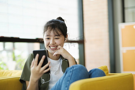 年轻的亚洲女人微笑着在家里使用智能手机听音乐。