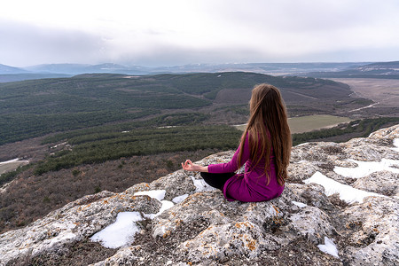 一个美丽的女人盘坐在高处的莲花位置上，可以欣赏到山脉和峡谷的壮丽景色，练习瑜伽冥想昆达里尼能量思维直觉普拉纳。