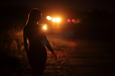 道路上汽车大灯背光中年轻苗条女性的剪影