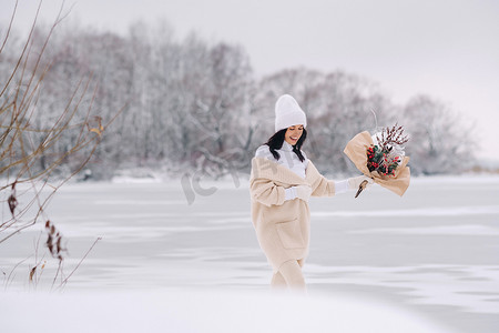 一个穿着米色开衫和冬花的女孩在下雪的季节在大自然中漫步。