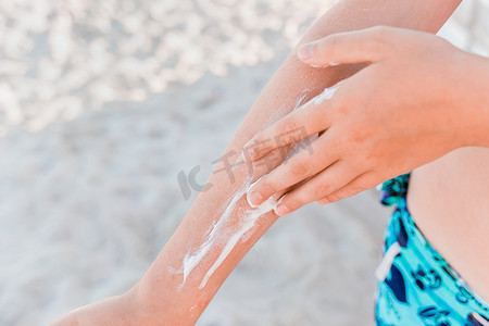 一个小女孩的手在海滩的背景下用二手涂抹防晒霜和防晒霜，特写