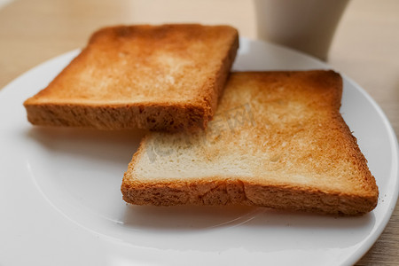 两片烤面包片放在白盘子上，咖啡放在木桌上，准备做早餐三明治。