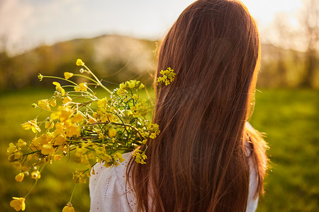 鲜花从摄影照片_从一位红发女子的背后拍摄的照片，在夕阳的光线下拿着一束鲜花