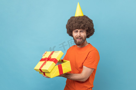 派对锥中悲伤不安的人拿着礼物盒，打开礼物，感到悲伤。
