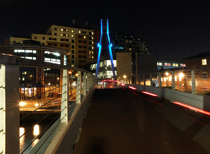 城市景观，人行天桥在夜间穿过利兹的艾尔河，灯光明亮，水边建筑和灯光小径