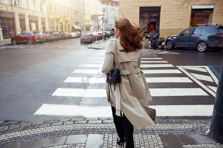 在城市建筑的背景下，穿着时髦服装的女性的背影穿过马路