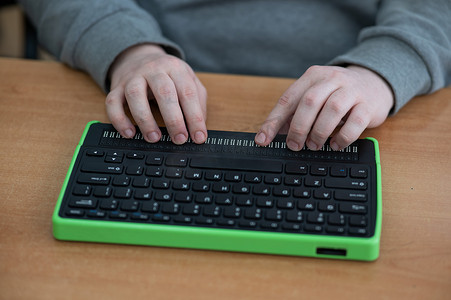 一位盲人使用带有盲文显示器和电脑键盘的电脑。