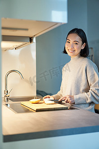 亚洲年轻女性做饭、做三明治、站在厨房时微笑的垂直照片