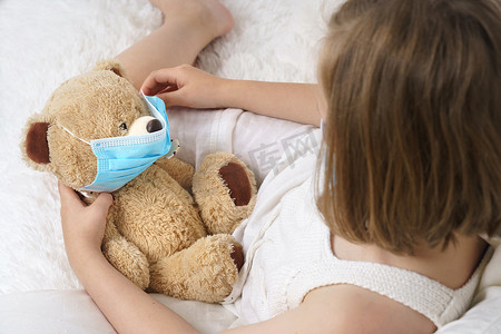 生病的少女为玩具戴上医用防护面具。