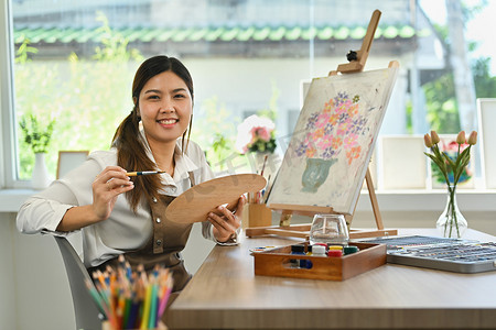 年轻亚洲家庭摄影照片_美丽的年轻亚洲女性享受创造力活动，在艺术工作室绘画。